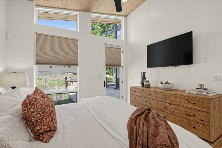 Bedroom with wood dresser, wall-mounted TV and forest windows